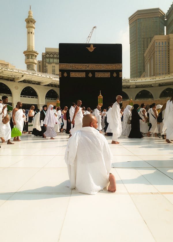 A pilgrim in ihram kneeling in prayer before the Kaaba at Masjid al-Haram